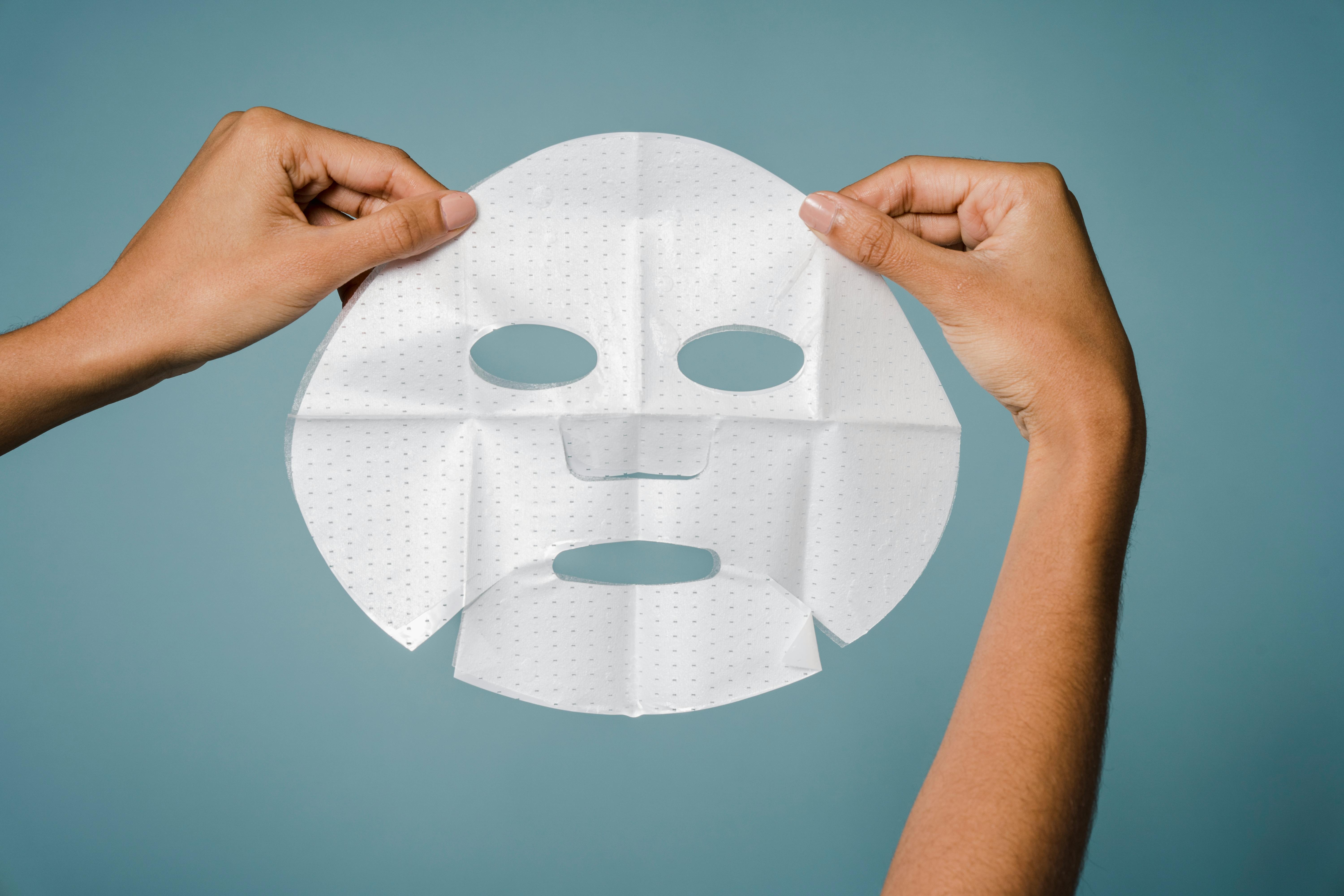 Crop anonymous woman demonstrating sheet mask in studio against blue background in daytime Crop anonymous woman demonstrating sheet mask in studio against blue background in daytime