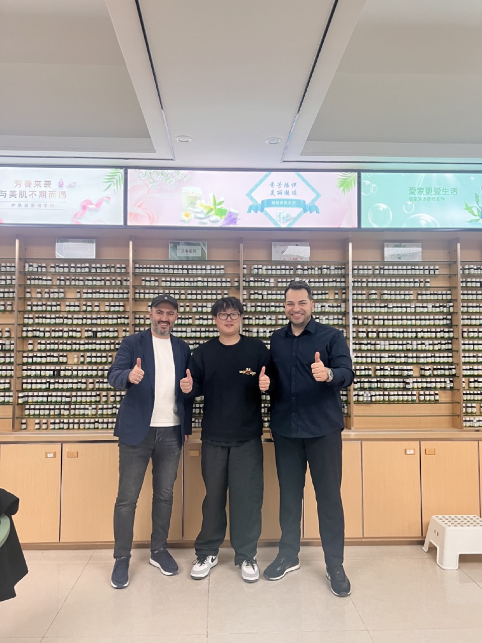 Three men giving thumbs up in front of a wall of essential oils.