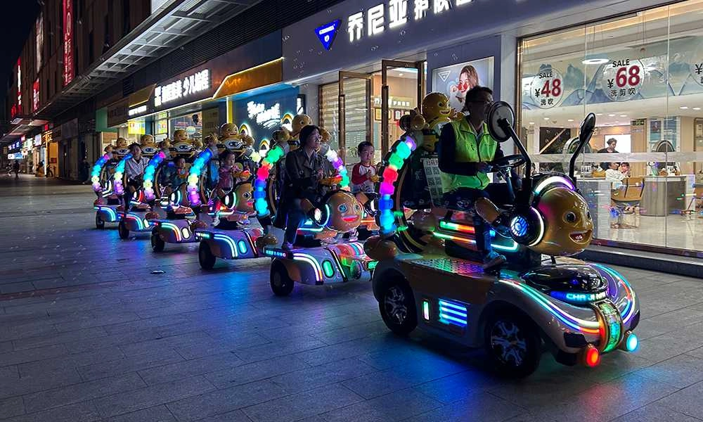 Children and adults ride nailong escort trackless train in front of shops at night - H.Q.Amusement