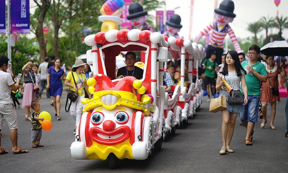 Clown-faced trackless train ride carrying passengers at an outdoor amusement park - H.Q.Amusement