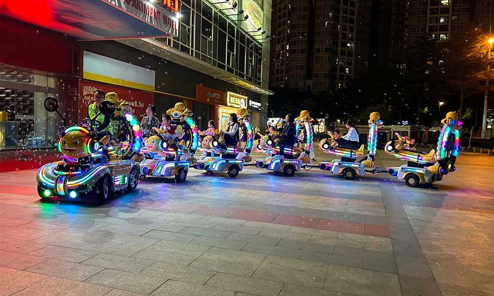 Light-up nailong escort trackless train with children and adults at night near a building - H.Q.Amusement