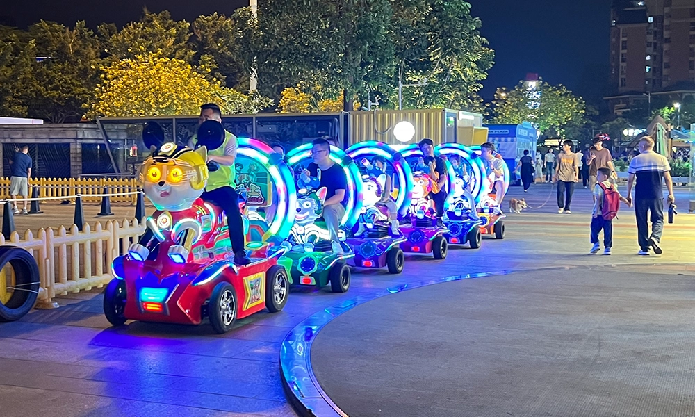 Nighttime view of nailong escort trackless train with colorful lights in a public park - H.Q.Amusement