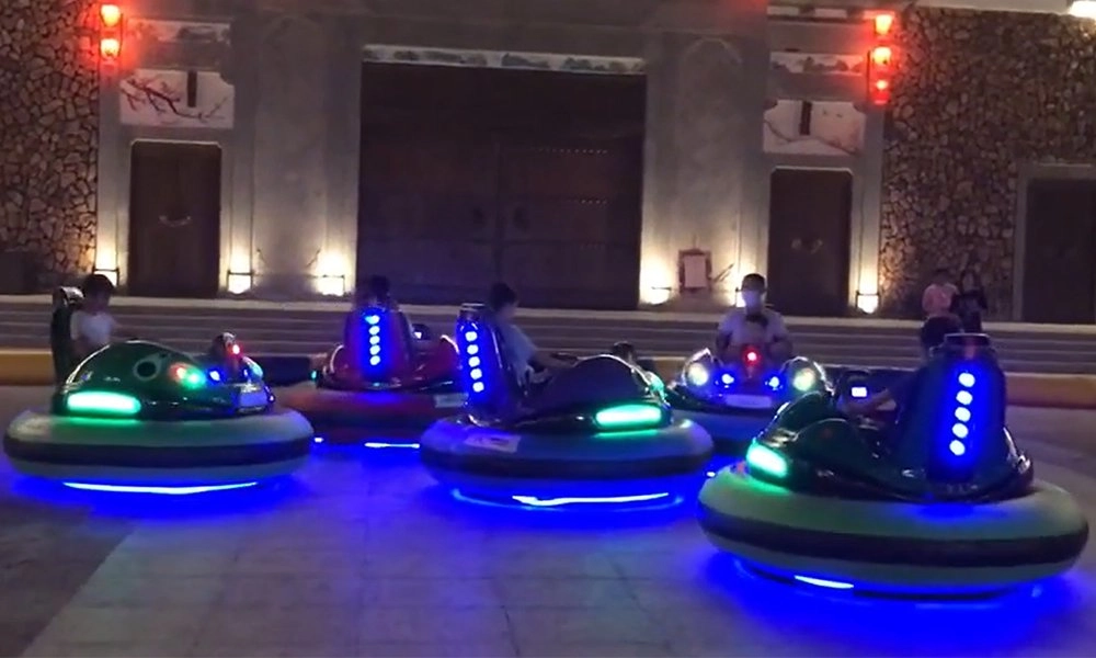 People riding illuminated bumper cars outdoors at night with a traditional building in the background - H.Q.Amusement