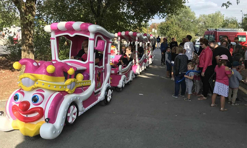 Pink and white clown-themed trackless train at outdoor amusement park - H.Q.Amusement