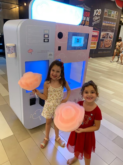 Two children holding cotton candy standing in front of the automatic cotton candy machine