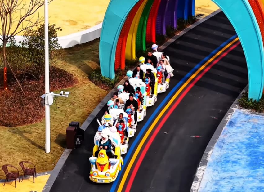 أشخاص يركبون قطارًا ملونًا من طراز "سونهونغ" في مدينة الملاهي، تحت قوس قزح، لعرض رحلة قطار بدون مسار مصممة خصيصًا للترفيه في مدن الملاهي والمعالم السياحية العائلية - سونهونغ