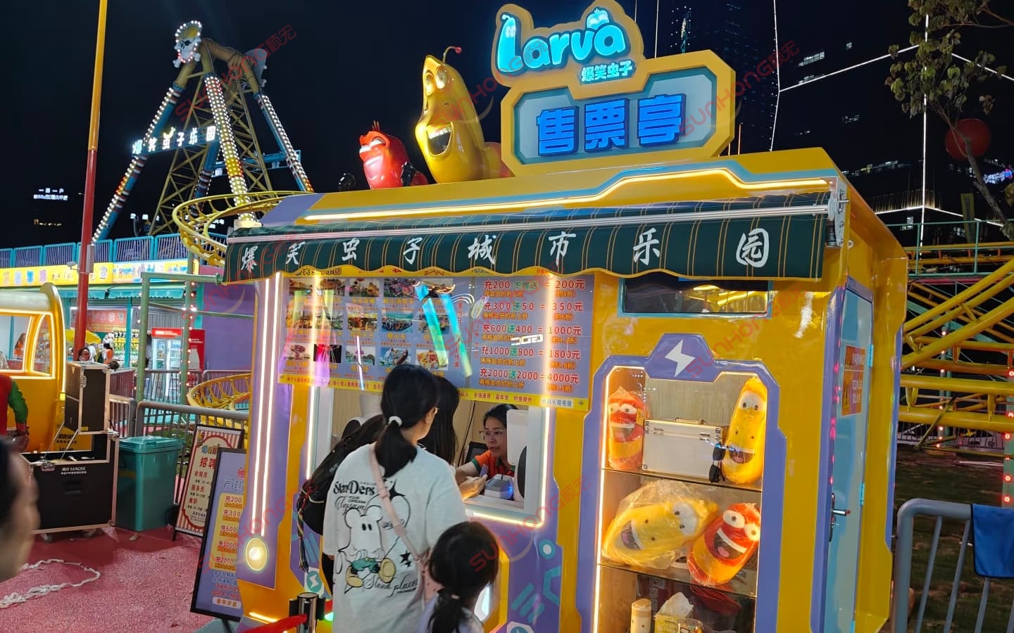 Night view of a brightly lit ticket booth at Larva themed amusement park with rides. Night view of a brightly lit ticket booth at