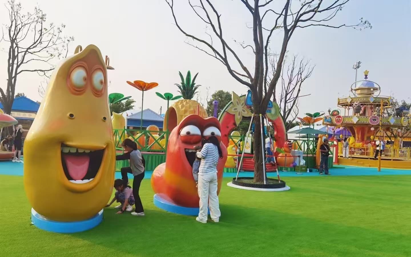 Kids playing around Larva cartoon character sculptures in an outdoor amusement park.