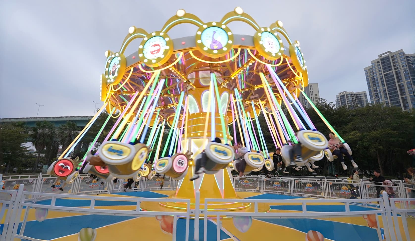 People enjoy Larva flying chair funfair amusement rides with colorful neon lights at dusk. - SUNHONG
