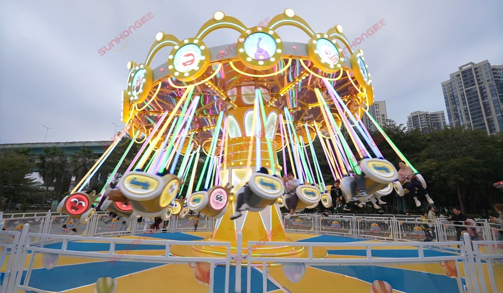 People enjoy Larva flying chair funfair amusement rides with colorful neon lights at dusk. People enjoy Larva flying chair funfair amusement rides with colorful neon lights at dusk.