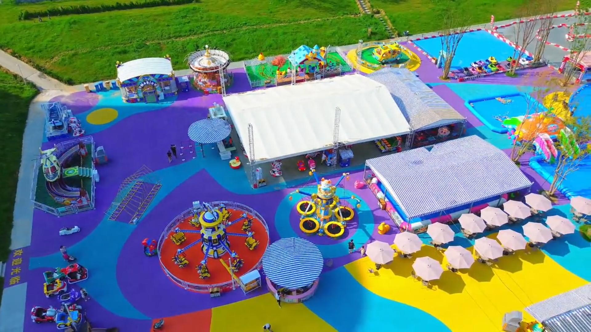 Aerial view of a colorful outdoor amusement park with various rides and tents.