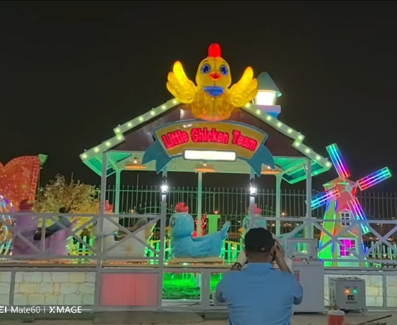 Manège illuminé « Little Chicken Team » dans un parc extérieur du Koweït, avec un design de poulet jaune lumineux. Mini-montagnes russes à vendre, vue nocturne. - SUNHONG