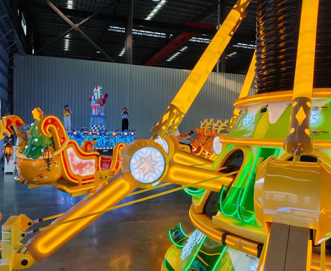 Bright yellow Christmas-themed amusement ride with sleigh-shaped cars at an outdoor theme park. - SUNHONG