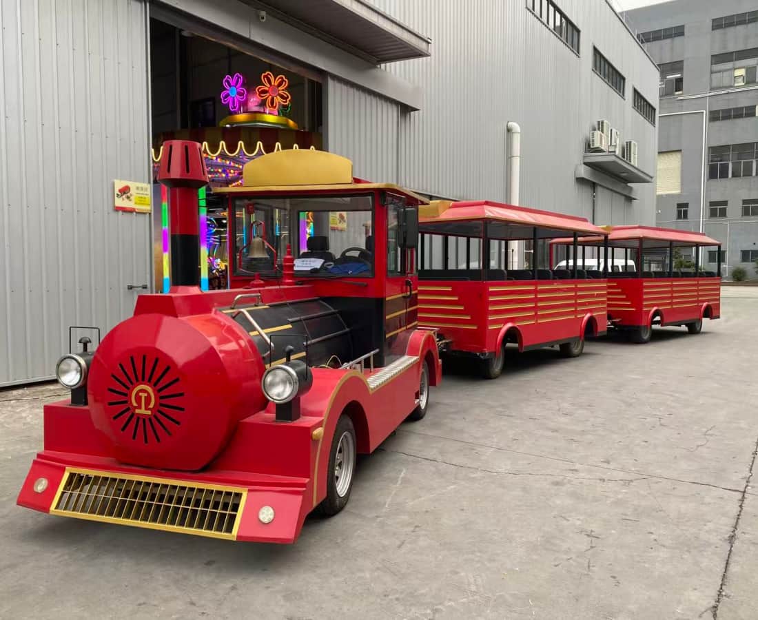 قطار SUNHONG الأحمر بدون مسارات، مخصص لرحلات المتنزهات الترفيهية، مزود بعربتين للركاب، متوقف خارج مبنى، مصمم خصيصًا لنقل الركاب في المتنزهات الترفيهية ورحلات القطارات الترفيهية - SUNHONG