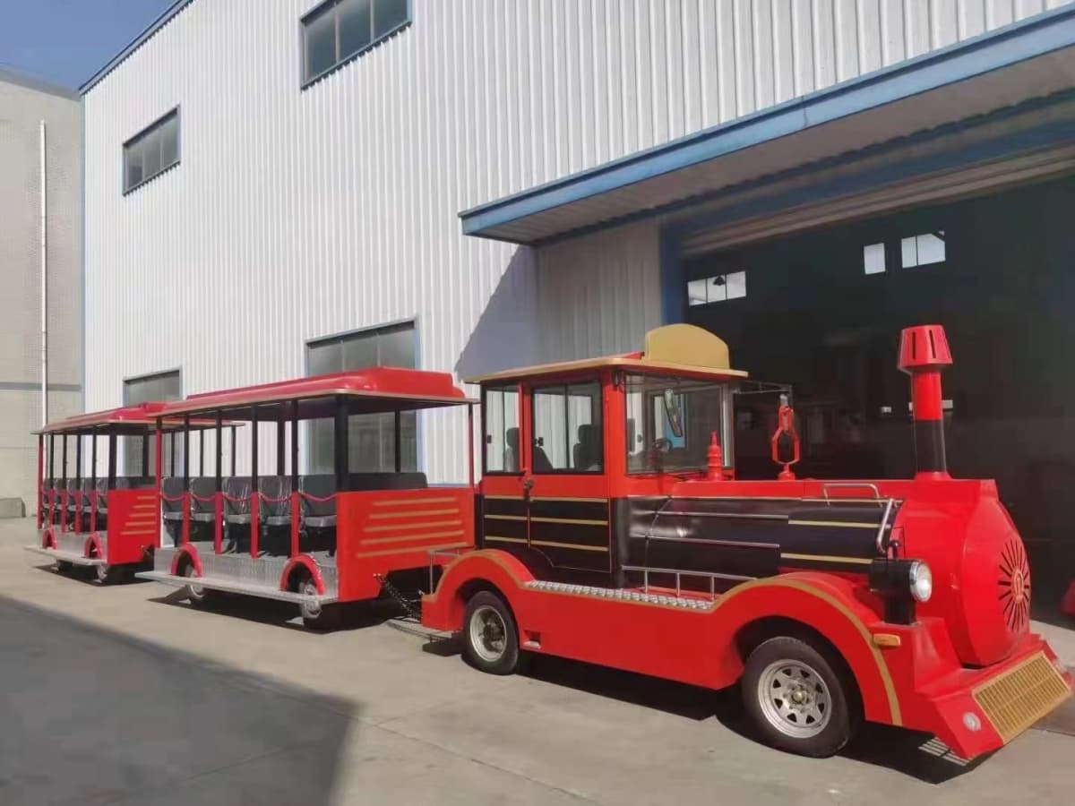 Kereta api taman hiburan merah dan hitam dengan kabin terbuka di luar kilang
