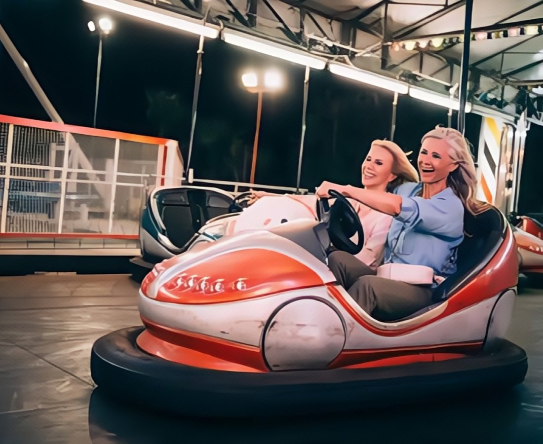 Two women are enjoying a ride in a red and white bumper car at an indoor amusement park. - SUNHONG
