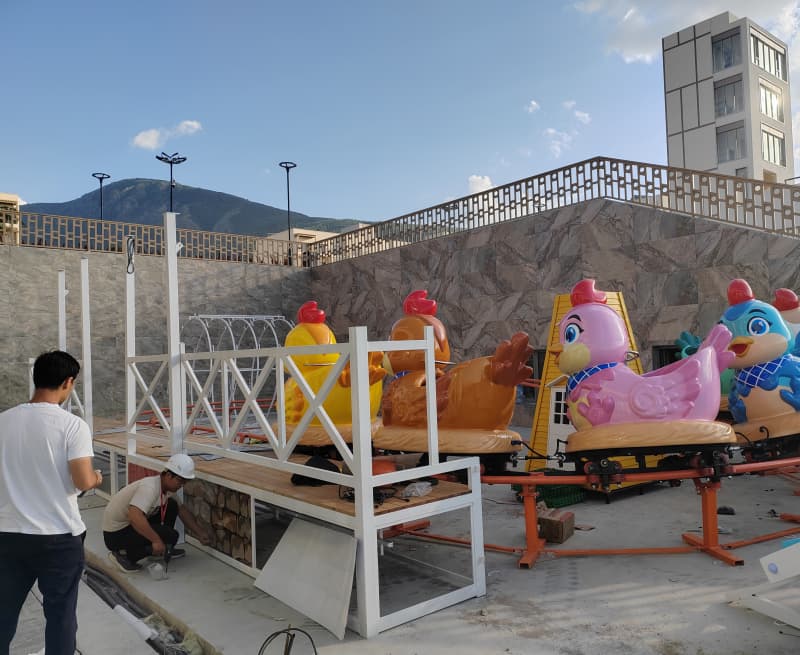 Des ouvriers installent un manège pour enfants coloré sur le thème des poulets dans un parc d'attractions d'une station balnéaire ouzbèke. Projet d'installation extérieure de mini-montagnes russes à vendre. - SUNHONG