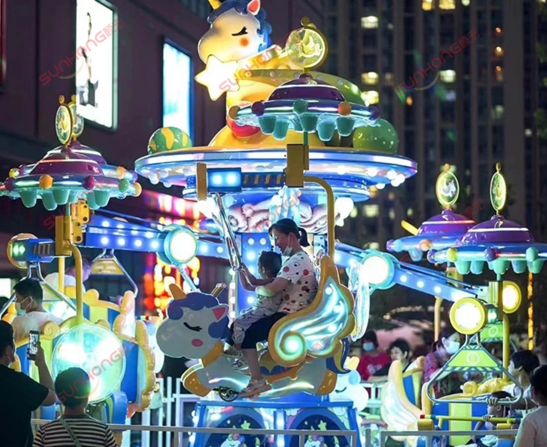 fairy-unicorn-ride-community-night - SUNHONG Families and children riding the Fairy Unicorn Amusement Ride at night in a lively community plaza, with glowing lights and playful design. - SUNHONG