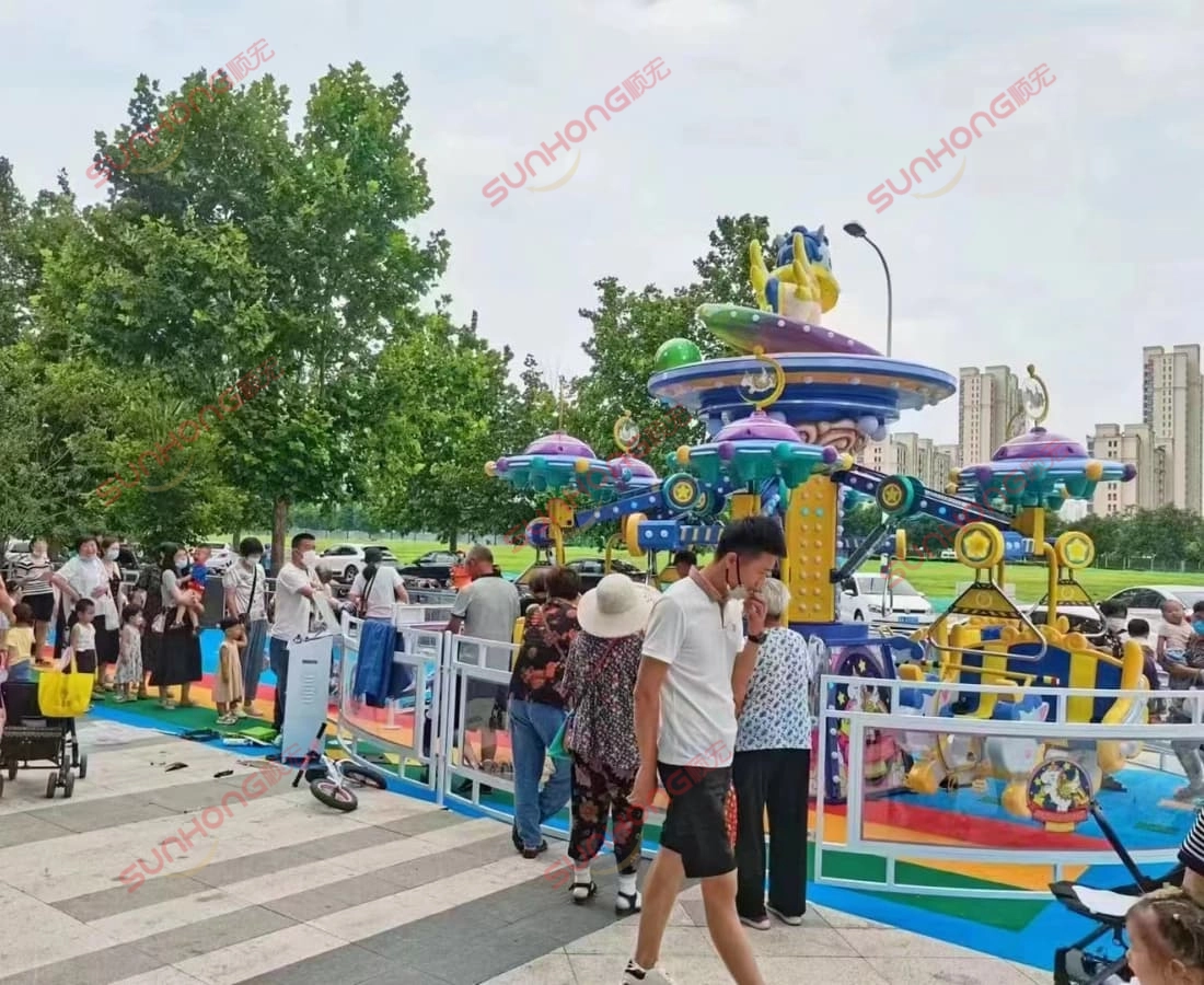 fairy-unicorn-ride-daytime-park-queue - SUNHONG Visitors queuing for the Fairy Unicorn Ride under daylight in an open plaza next to trees and residential buildings. - SUNHONG