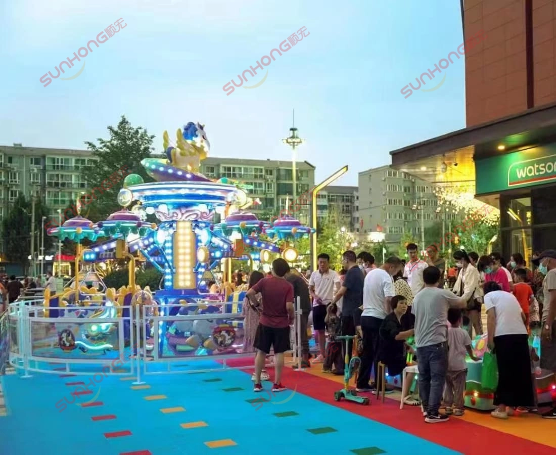 fairy-unicorn-ride-evening-queue-watsons - SUNHONG Crowds gathering at dusk around the lit-up Fairy Unicorn Ride outside a Watsons store, showing growing excitement and popularity. - SUNHONG