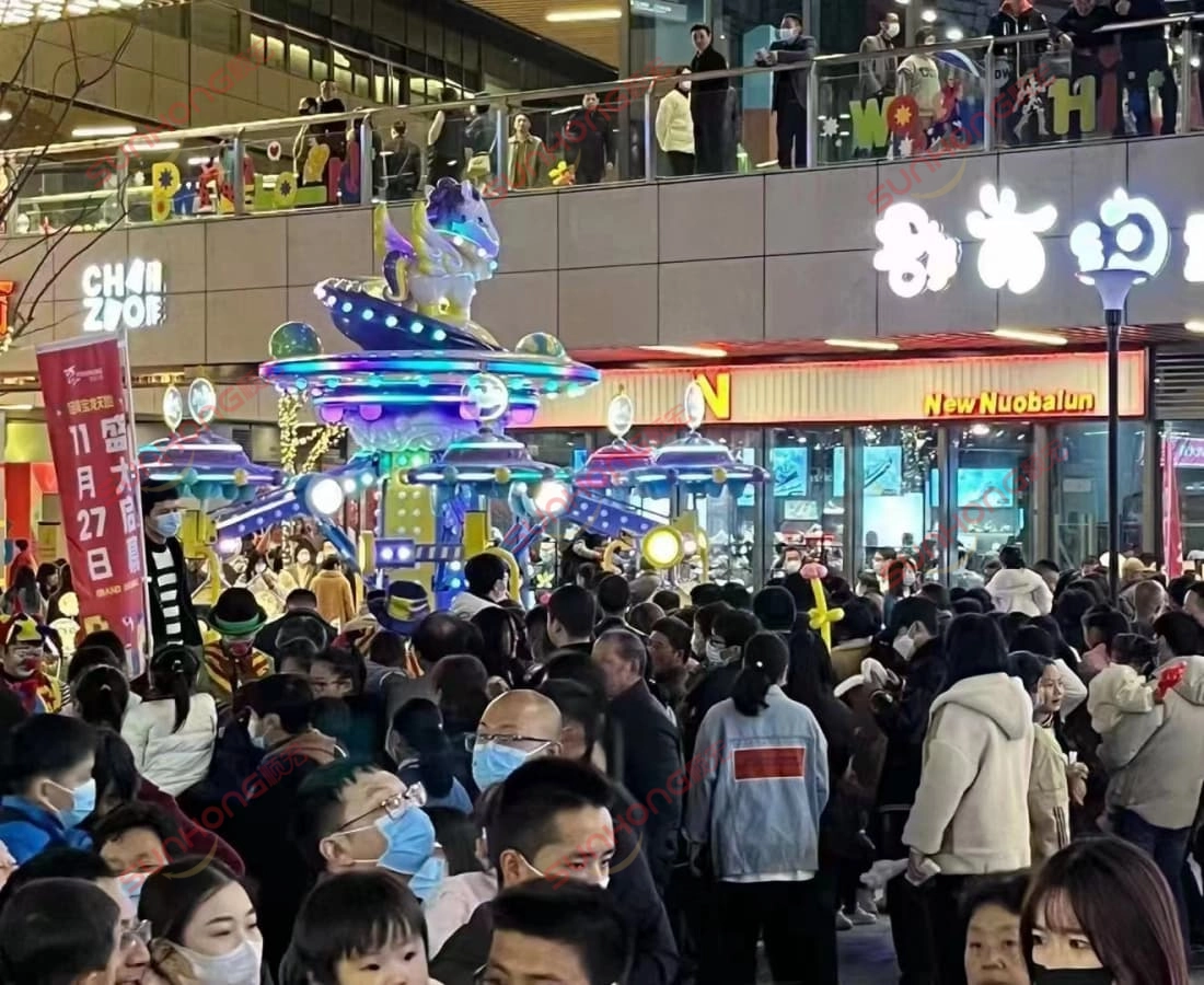 fairy-unicorn-ride-night-crowd-mall - SUNHONG Large crowd gathered around the Fairy Unicorn Ride outside a shopping mall at night, showing high popularity and festive atmosphere. - SUNHONG