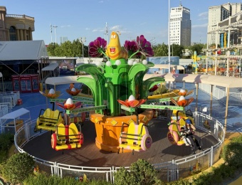 Brinquedo de parque de diversões com uma planta verde gigante e um personagem de inseto, assentos amarelos e passageiros. - SUNHONG