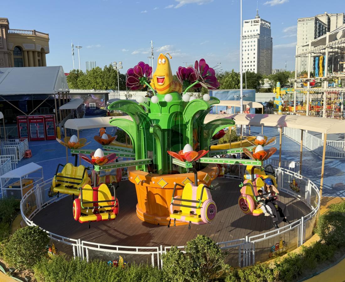 Real-life photo of the Larva Blooms amusement ride at a Larva-themed park, with the amusement park in the background