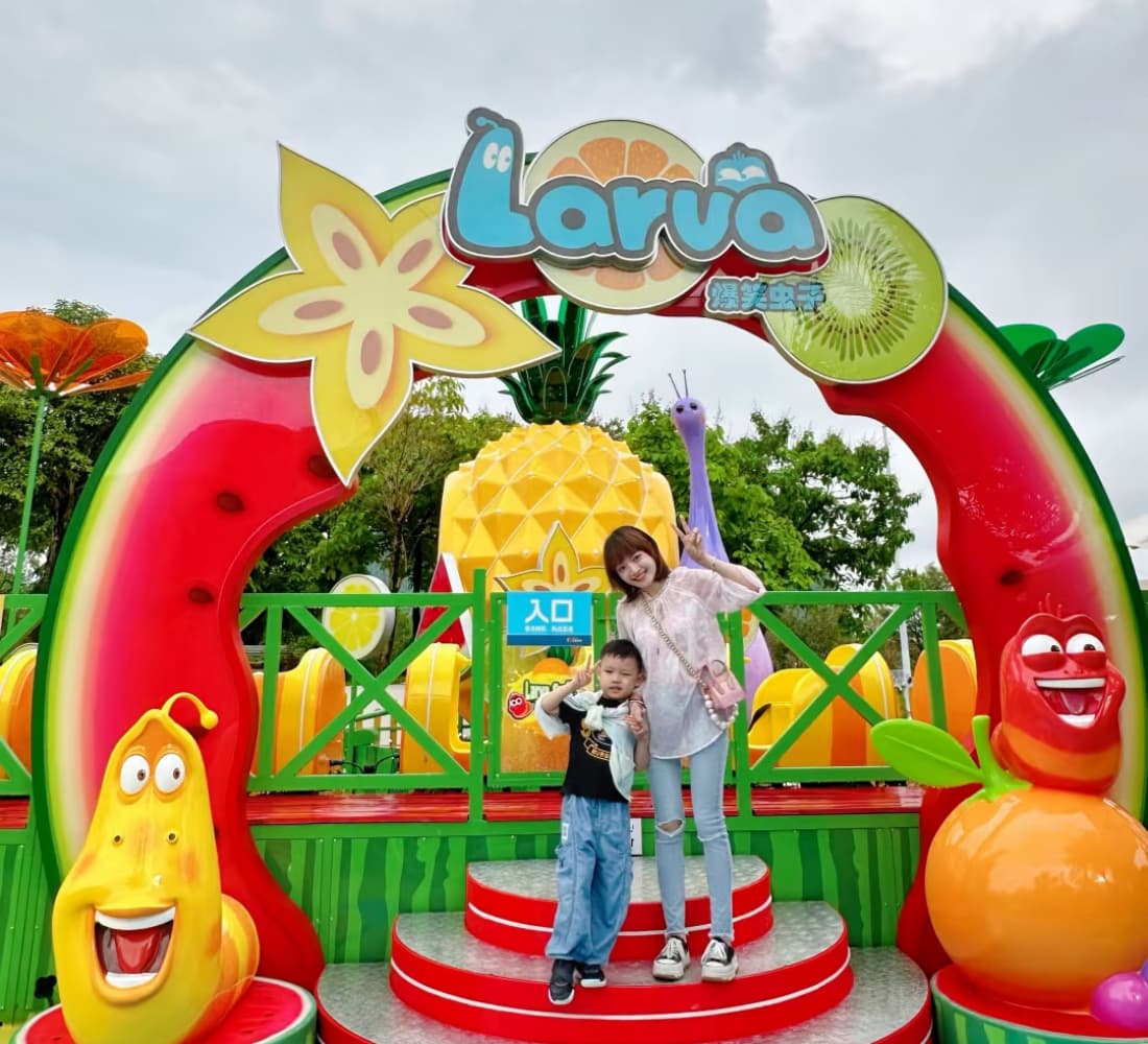 Family posing at the entrance of Larva Fruitland mini roller coaster under fruit-themed archway. - SUNHONG