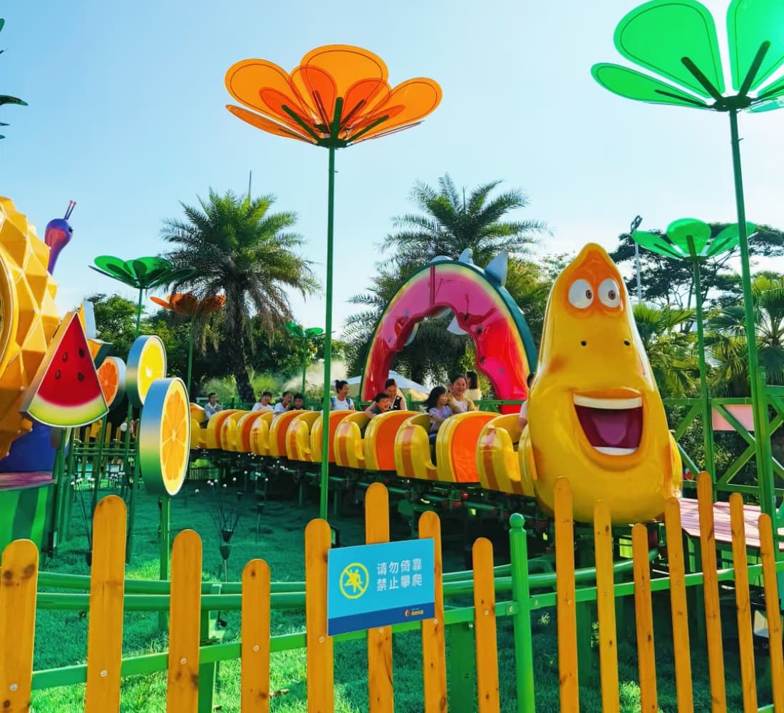 Children riding the Larva Fruitland mini roller coaster surrounded by vibrant fruit and flower decorations. - SUNHONG