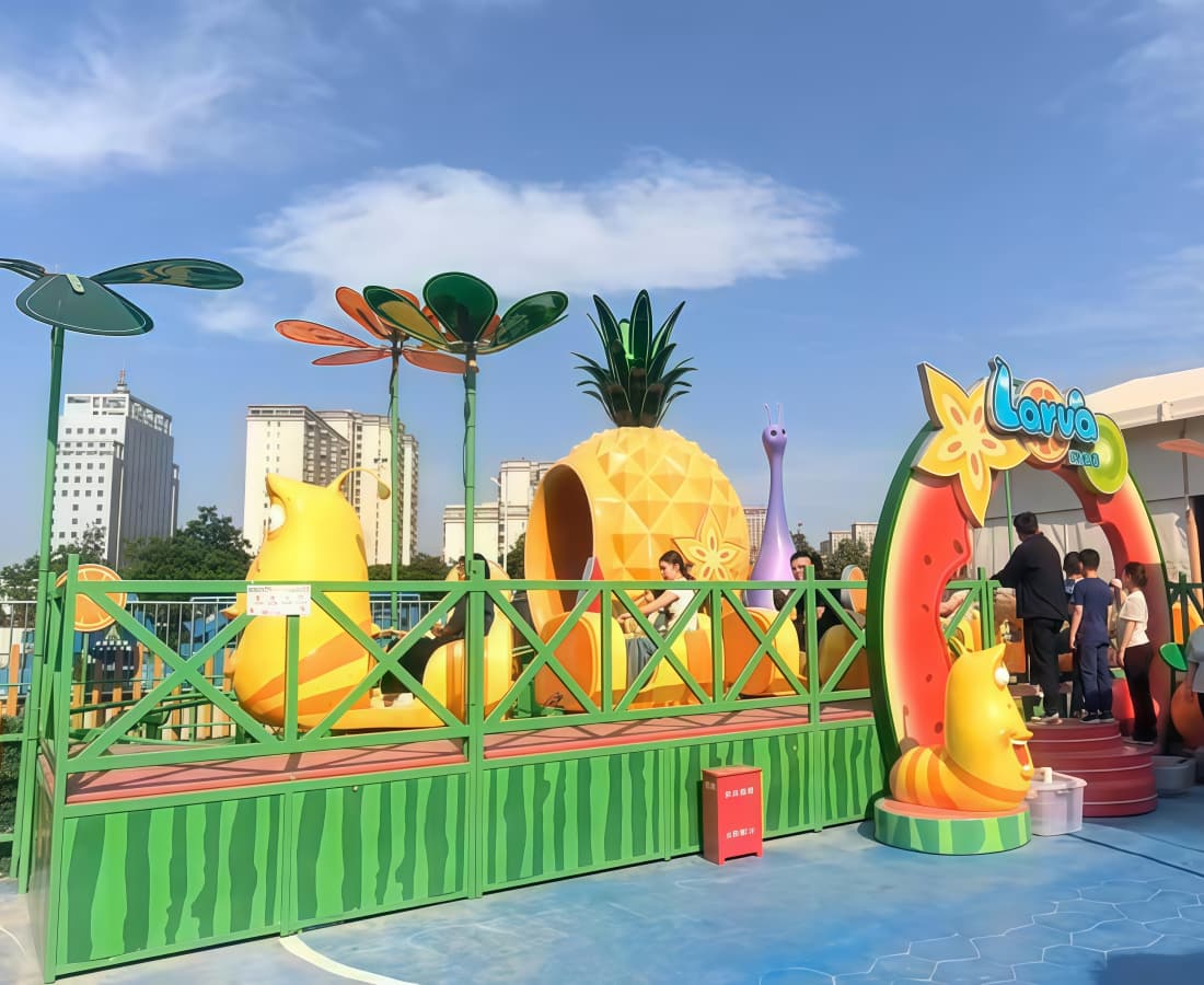 Larva Fruitland mini coaster in a park, with full seats and guests lining up at the entrance. - SUNHONG