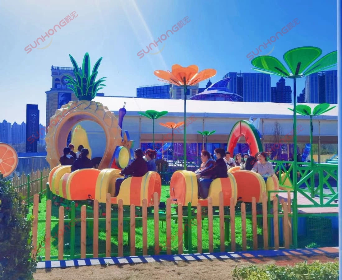larva-fruitland-mini-roller-coaster-sunny-yellow-track - SUNHONG Larva Fruitland mini roller coaster running under sunlight with kids onboard, showing Yellow front car and green track. - SUNHONG