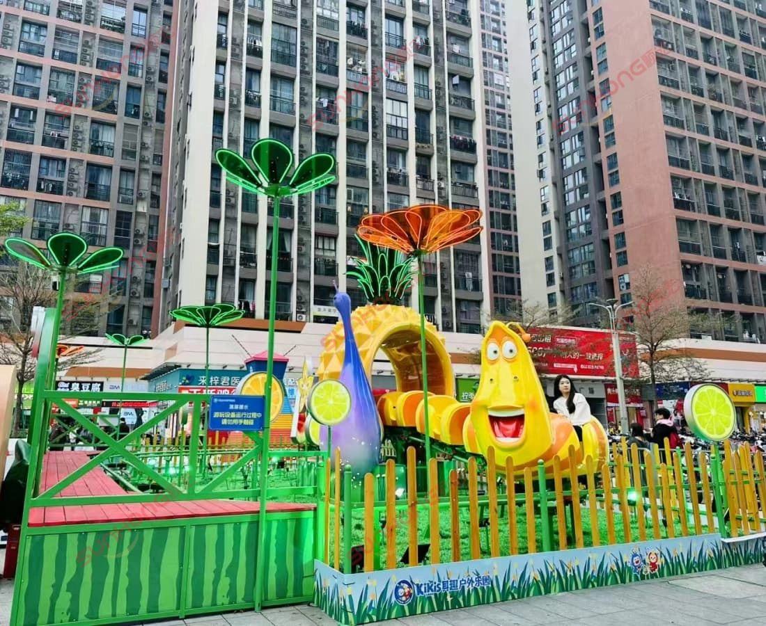 larva-fruitland-small-coaster-community-girl-riding - SUNHONG Girl enjoying Larva Fruitland small coaster in a sunny community plaza setting - SUNHONG