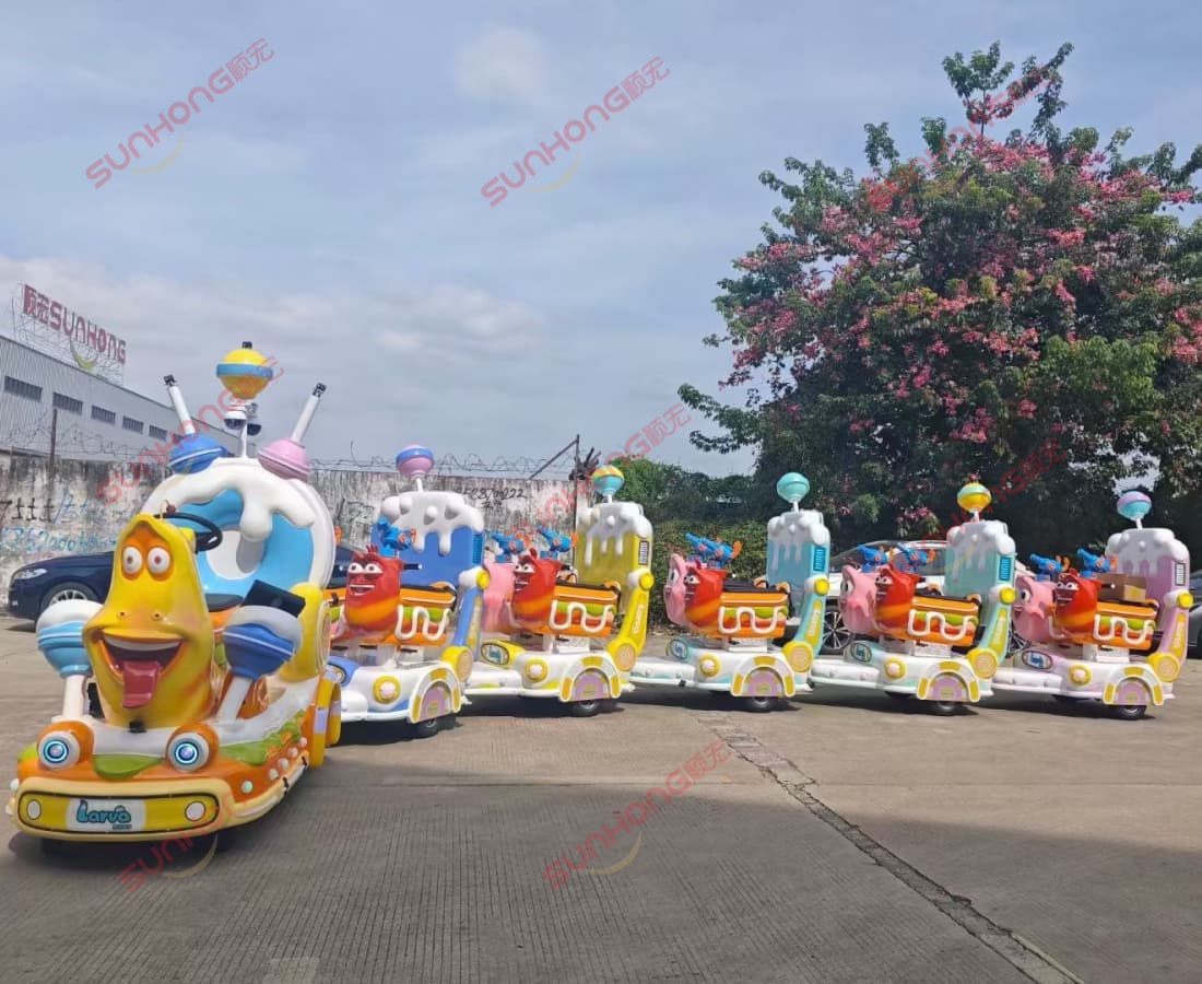 يرقة حارس قطار بلا مسار - سونهونغ - واجهة مصنع - أصفر - أحمر يتم عرض رحلة قطار Larva Ranger بدون مسار للبيع أمام مصنع SUNHONG، وتتميز بشخصيات صفراء وحمراء مع شعار SUNHONG في الخلفية.