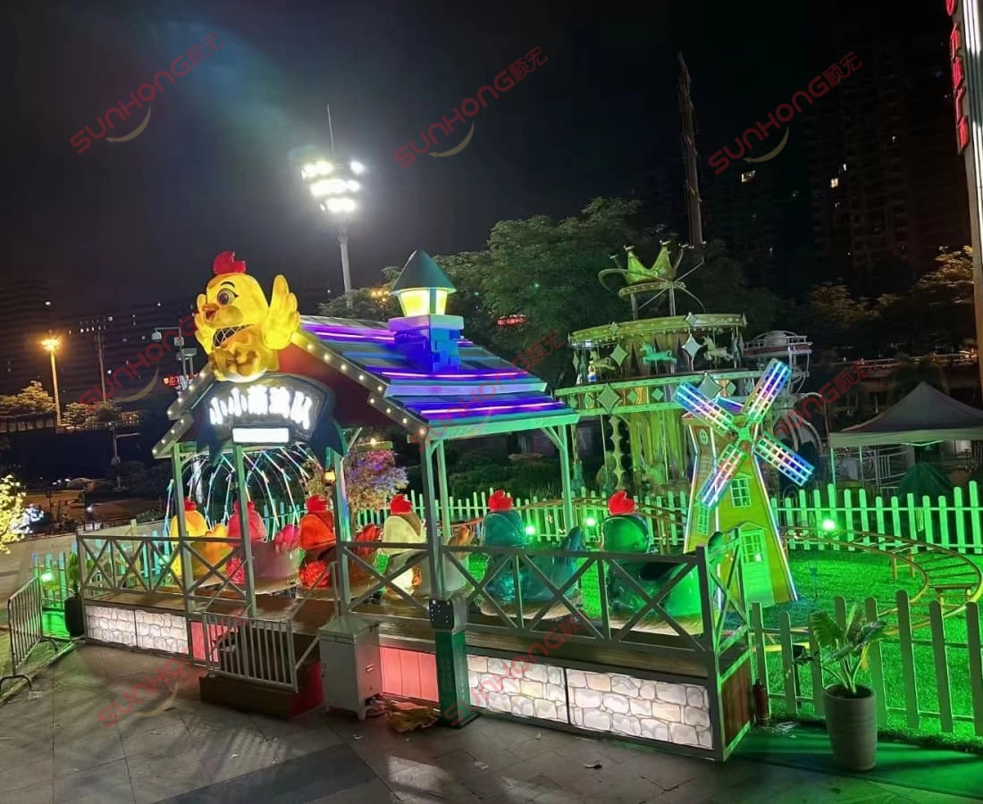 little-chicken-kiddie-coaster-night-city-lights - SUNHONG Night view of Little Chicken kiddie coaster ride with glowing chicken cars and vibrant lights in city square - SUNHONG