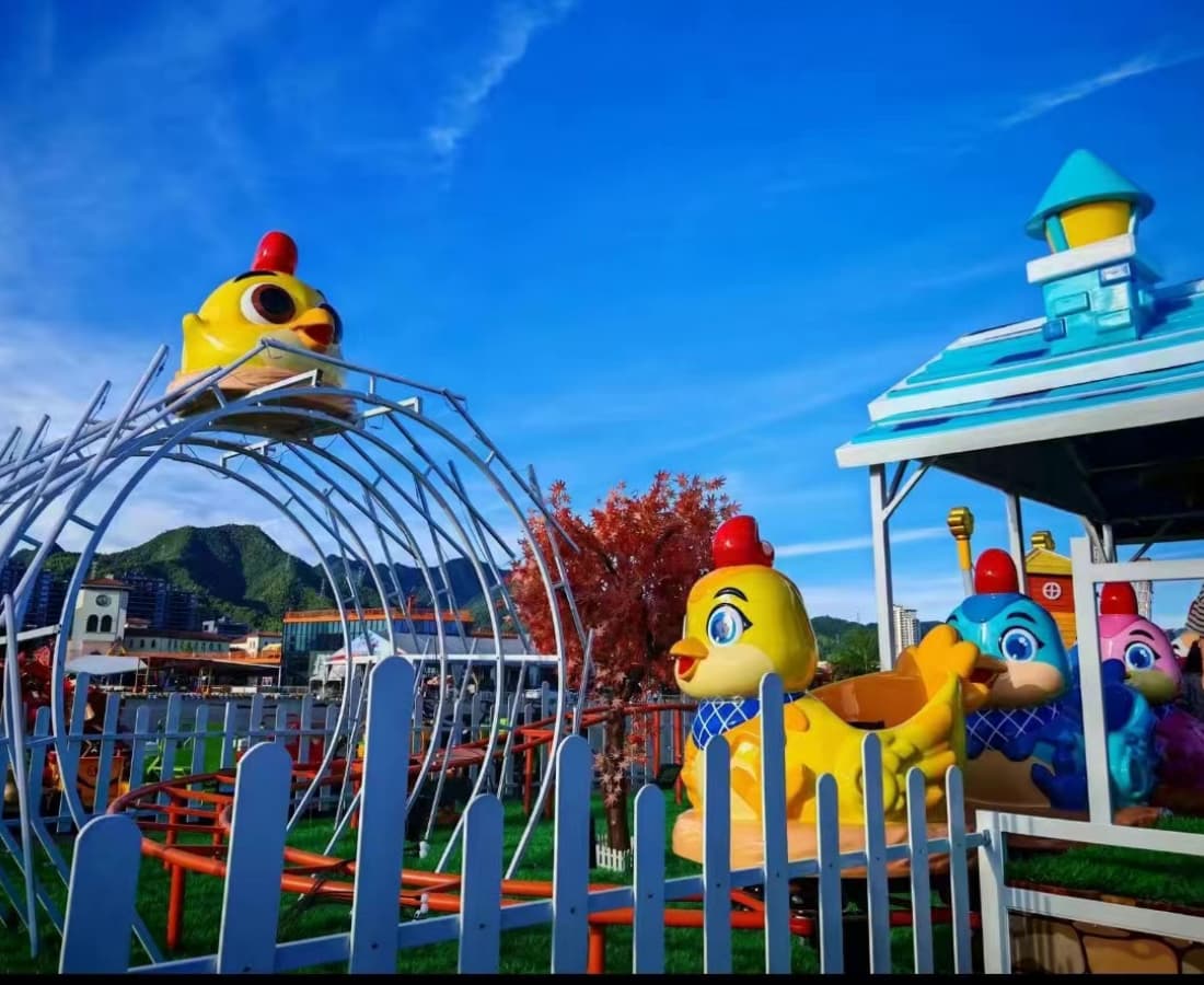Real-life image of Little Chicken Team kiddie coaster with yellow chicken train and scenic background - SUNHONG