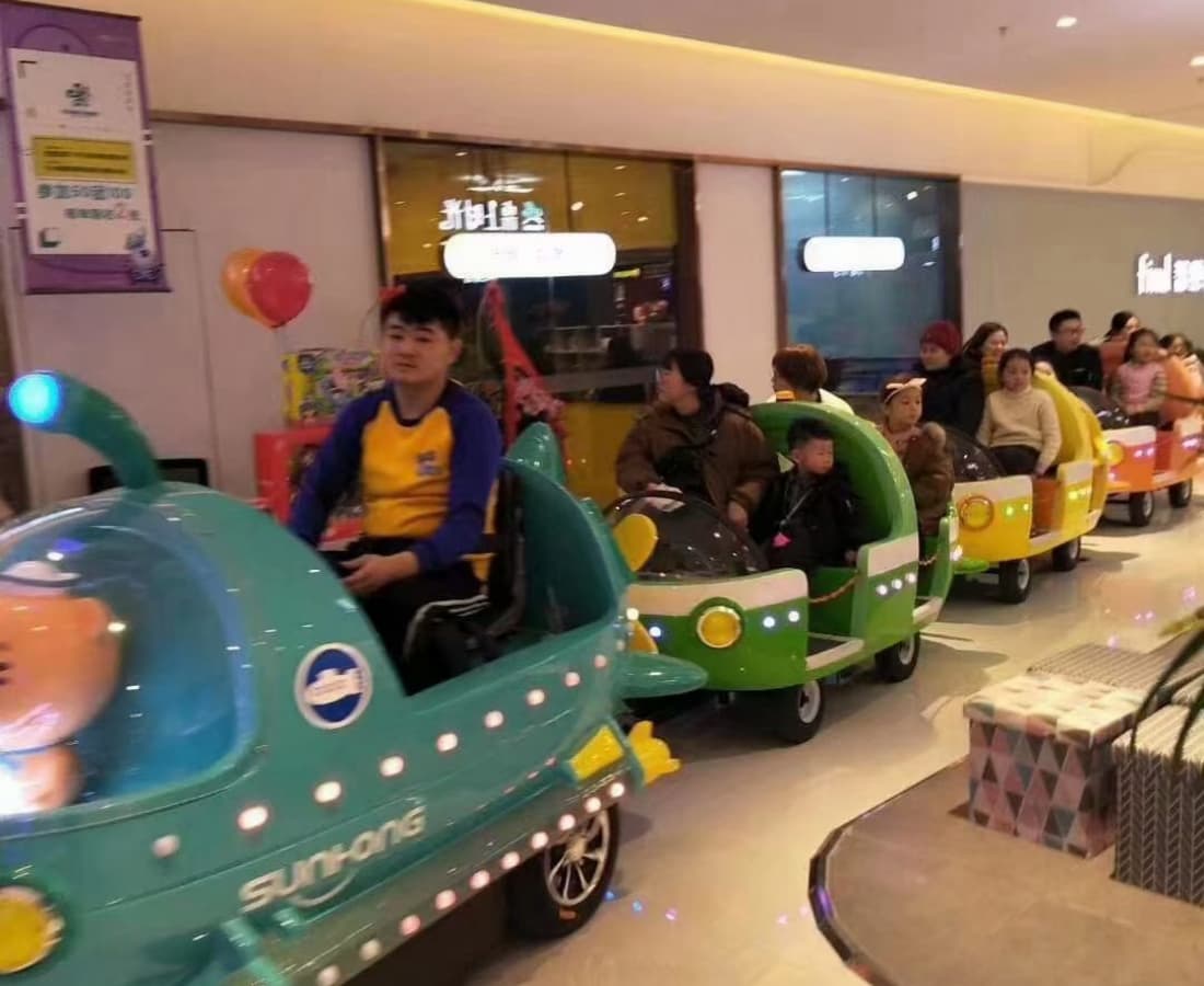 Trem elétrico sem trilhos com capacidade total para crianças circulando por um shopping com famílias a bordo. - SUNHONG