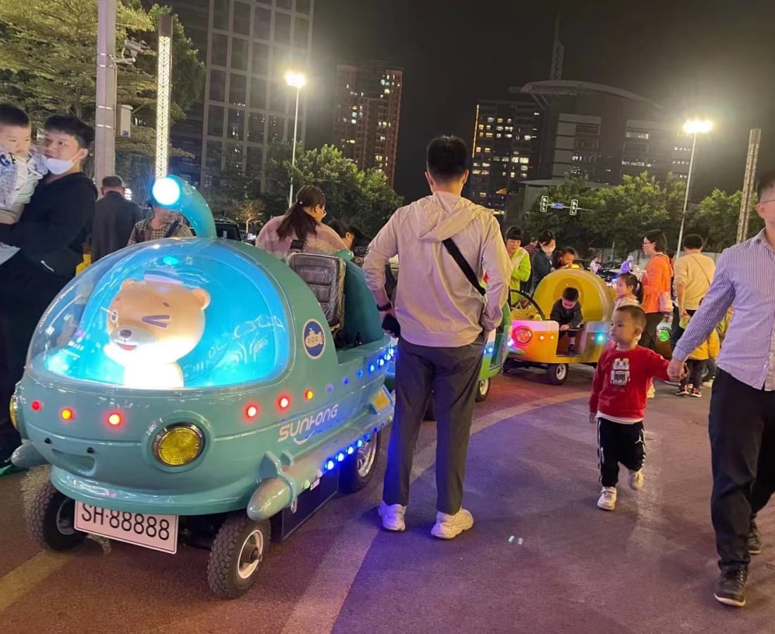 Trem elétrico sem trilhos para crianças, operando à noite em uma praça da cidade, com design e efeitos de iluminação com tema oceânico. - SUNHONG