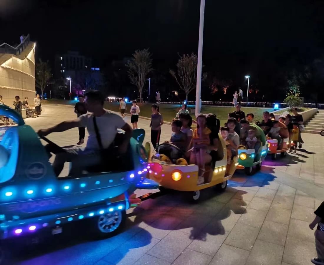 Trem oceânico elétrico sem trilhos operando ao ar livre em um parque à noite, lotado de crianças. - SUNHONG