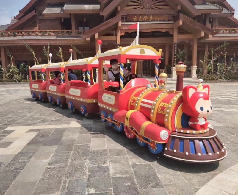 قطار SUNHONG الأحمر المخصص للأطفال، والمُزيّن بشخصية ثعلب كرتونية، ينقل الركاب أمام مبنى في بيئة مدينة ملاهي - SUNHONG