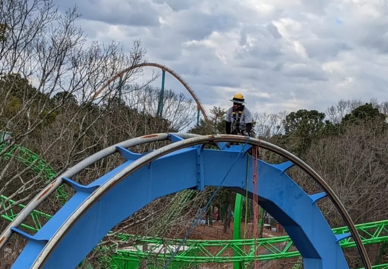 Technician performing high-altitude ride maintenance on a steel roller coaster to ensure structural integrity
