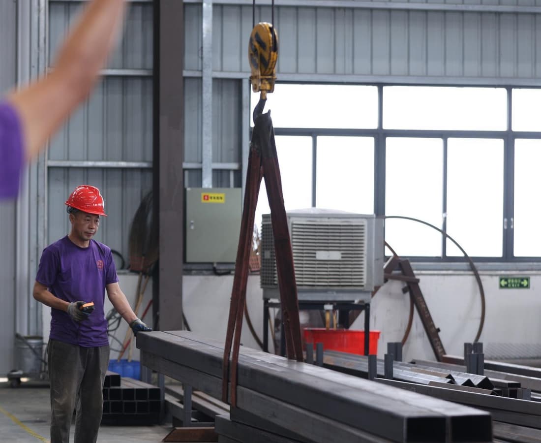 Рабочие производства компании SUNHONG с точностью и безопасностью перемещают сталь марки Q235B, используемую для изготовления компонентов аттракционов. - SUNHONG