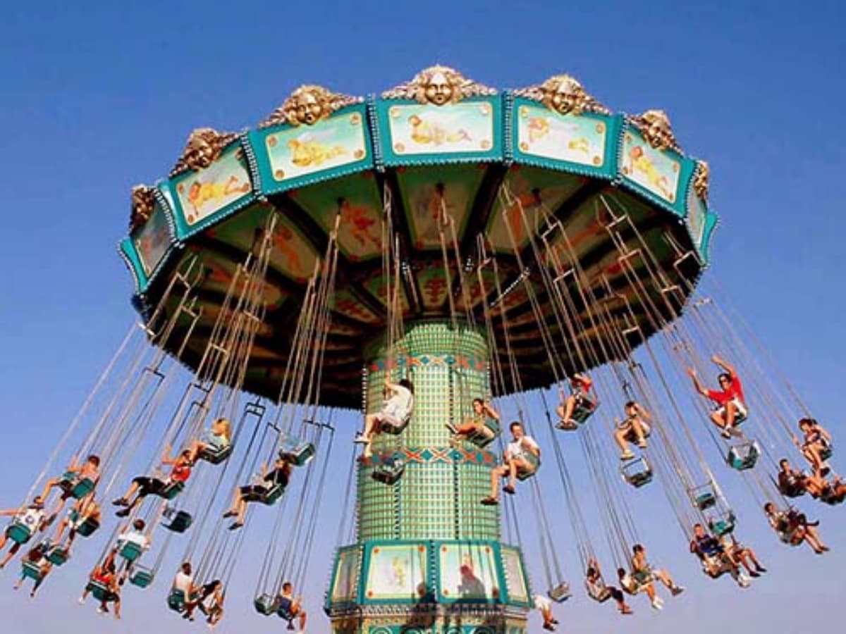 Close-up of riders on a swing fairground ride with striped colorful canopy.