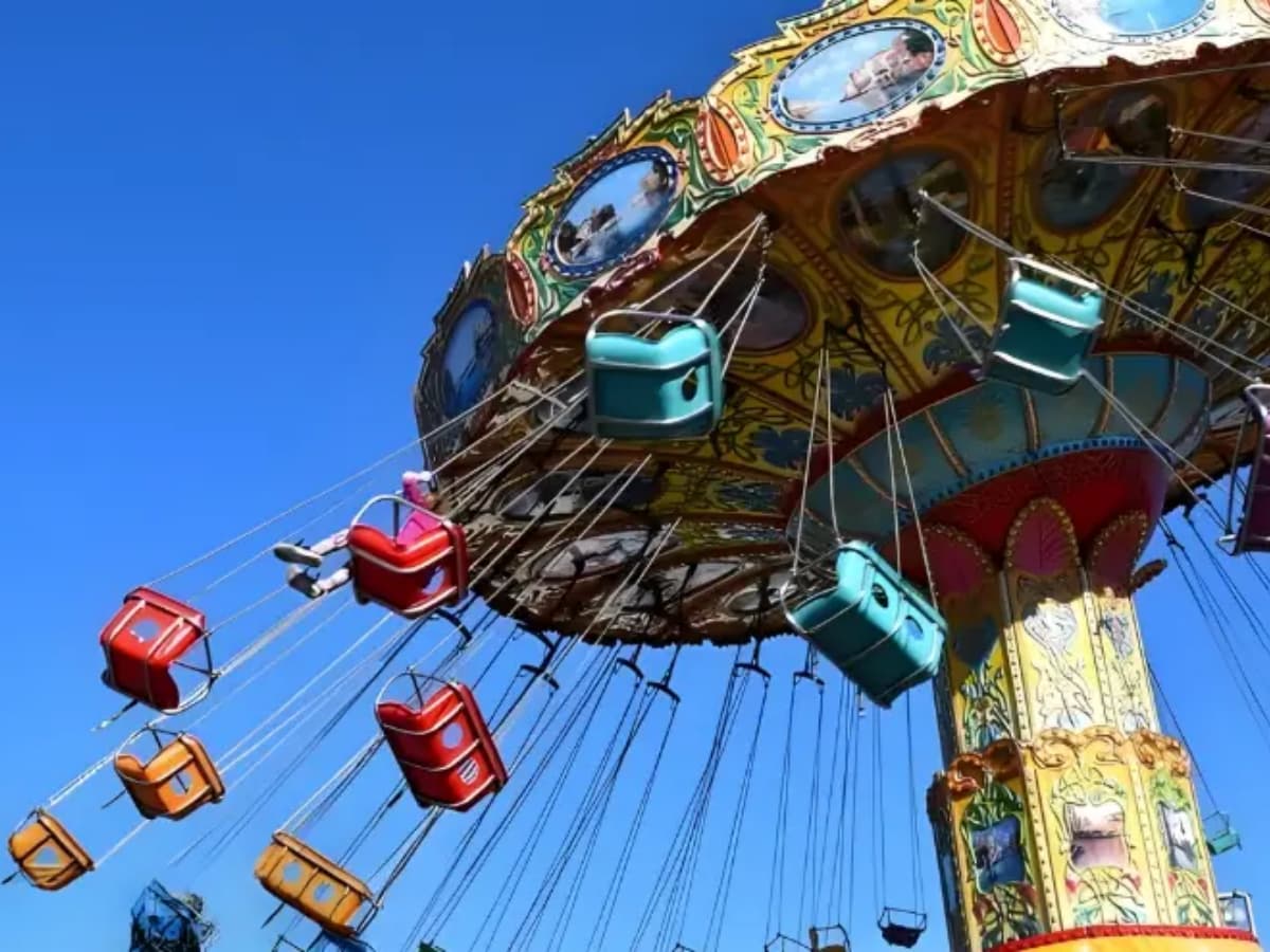 Swing ride at a funfair with green seats and clear blue sky background.