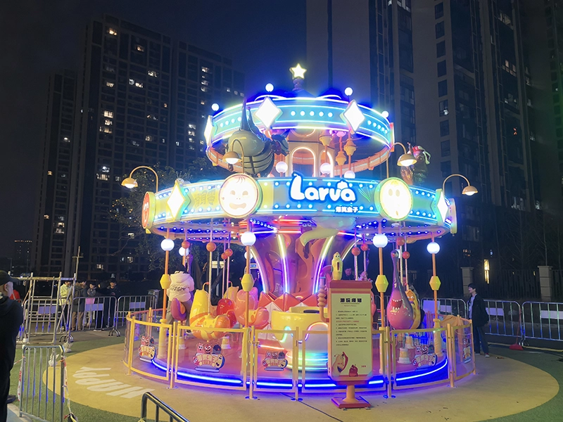 El carrusel de dos pisos Larva con 16 asientos brilla en el parque de atracciones por la noche.