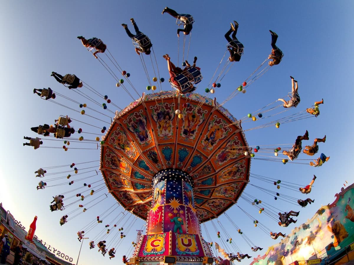The swings carnival ride with vibrant decorations and people flying under blue skies.