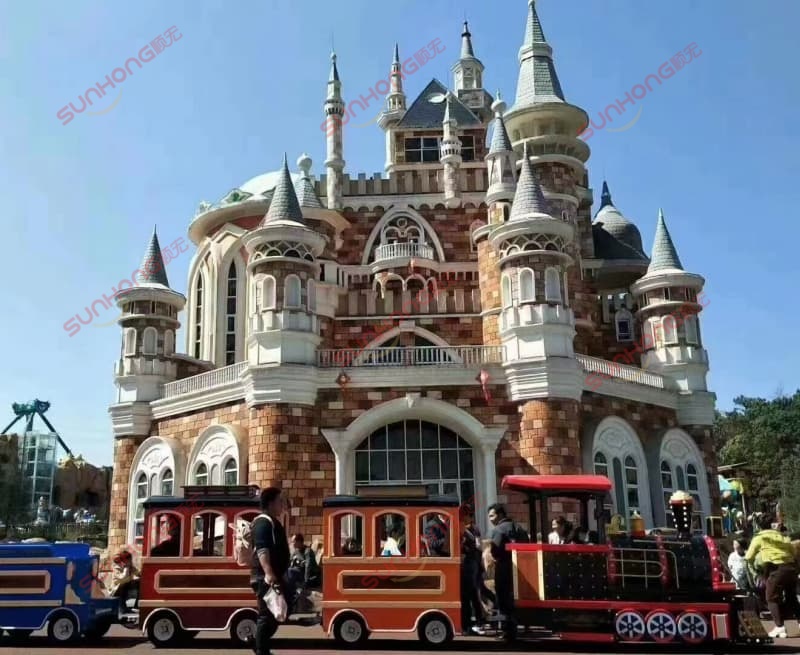 sunhong-amusement-park-train-ride-castle-mini-train-theme-park A miniature SUNHONG amusement park train ride operating in front of a castle inside a theme park, with visitors enjoying the attraction and entertainment environment