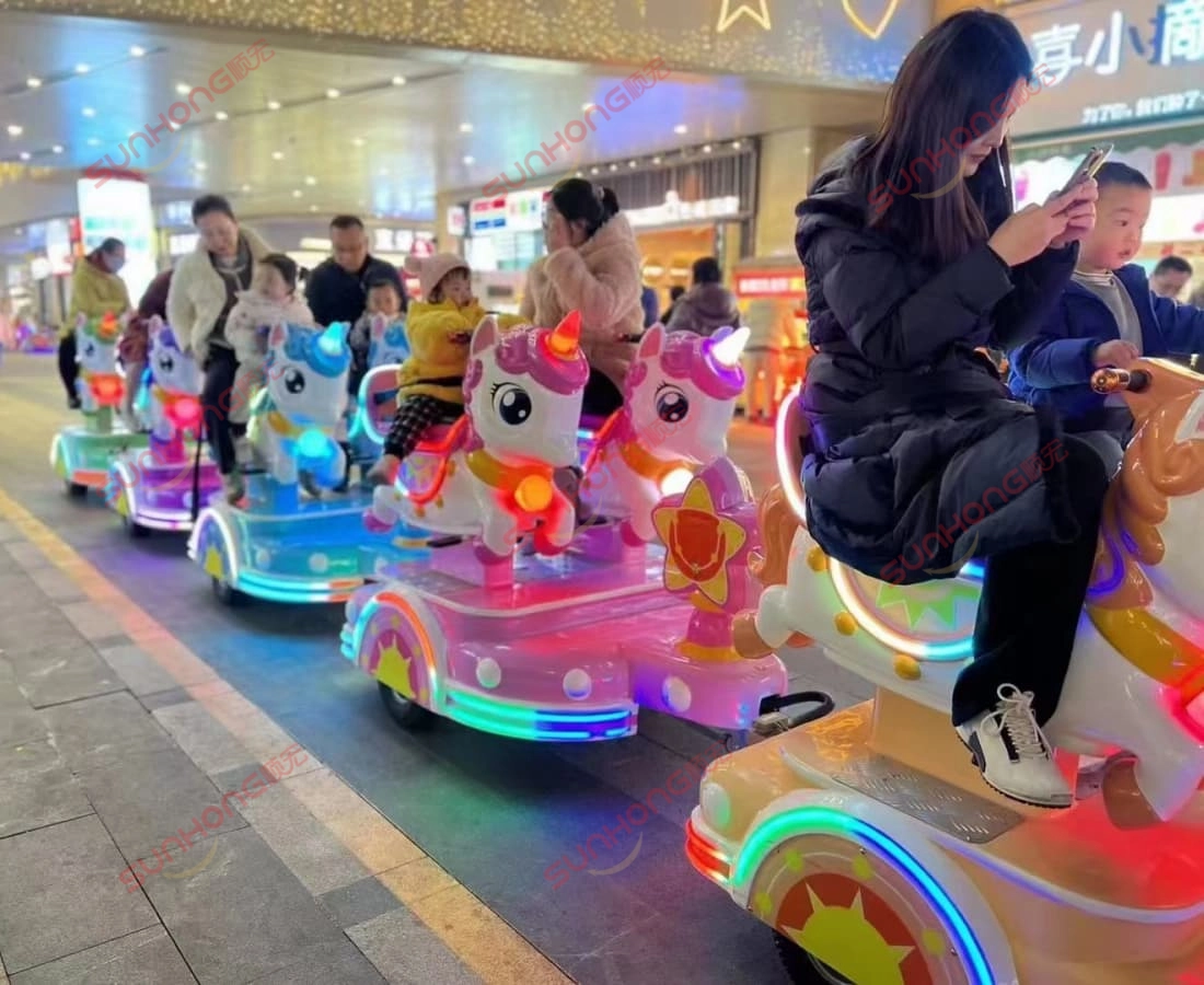 unicorn-kiddie-train-ride-outdoor-night-colorful - SUNHONG Kanak-kanak dan ibu bapa menikmati perjalanan kereta api unicorn kiddie di bawah lampu berwarna-warni dalam suasana malam luar. - SUNHONG