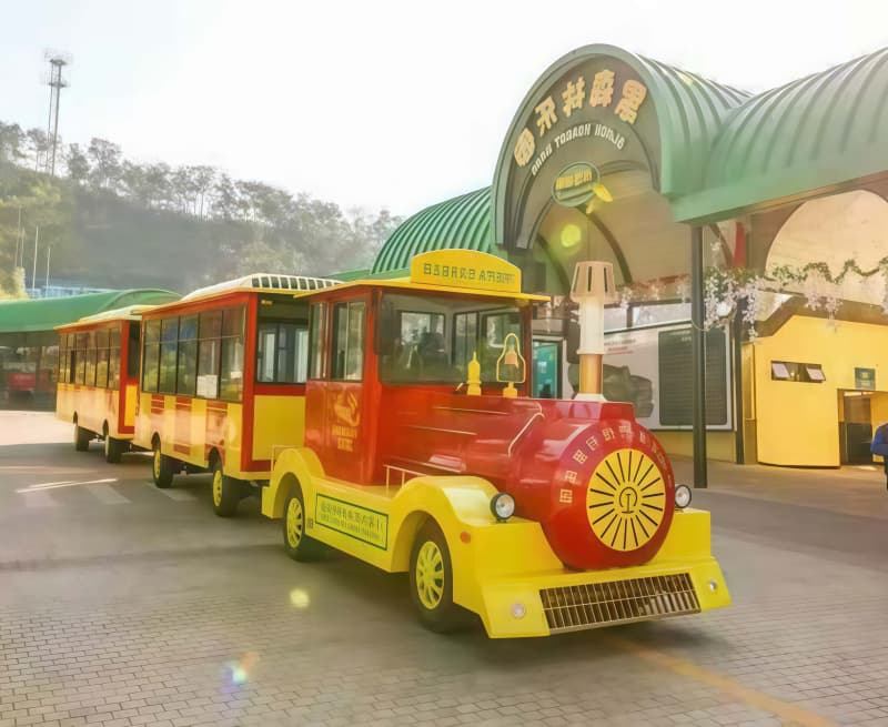 قطار منتزه سونهونغ السياحي ذو اللونين الأحمر والأصفر، يتألف من عربتين، يعمل أمام مبنى أخضر مقوس في بيئة منتزه ترفيهي - سونهونغ