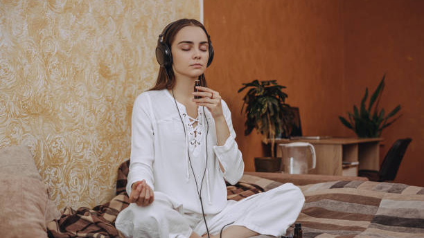 Woman in white meditating, using headphones and yoga oil for aromatherapy. Woman in white meditating, using headphones and yoga oil for aromatherapy.