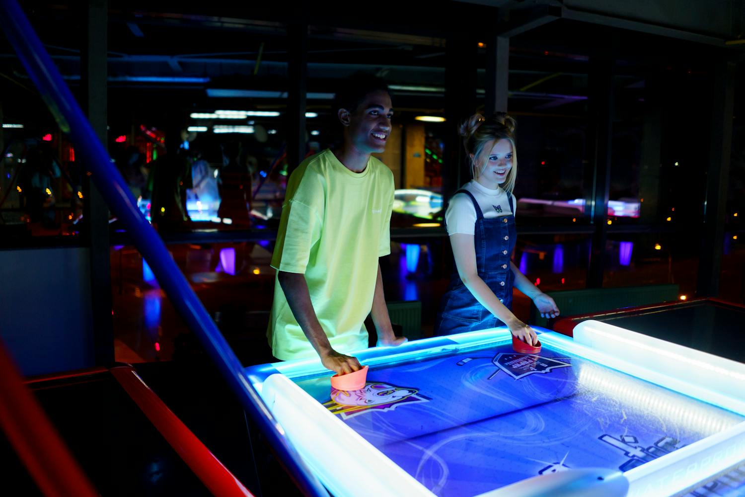 Ein junger Mann und eine junge Frau spielen Airhockey in einer hell erleuchteten Spielhalle.